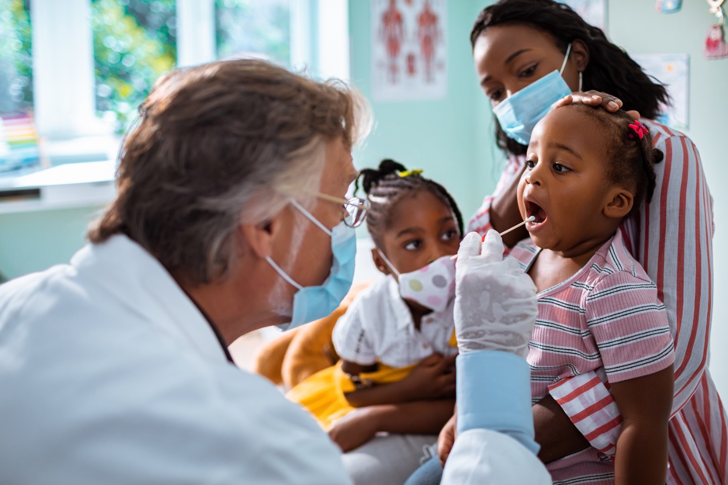 Doctor examining a young child with mom and sister looking on